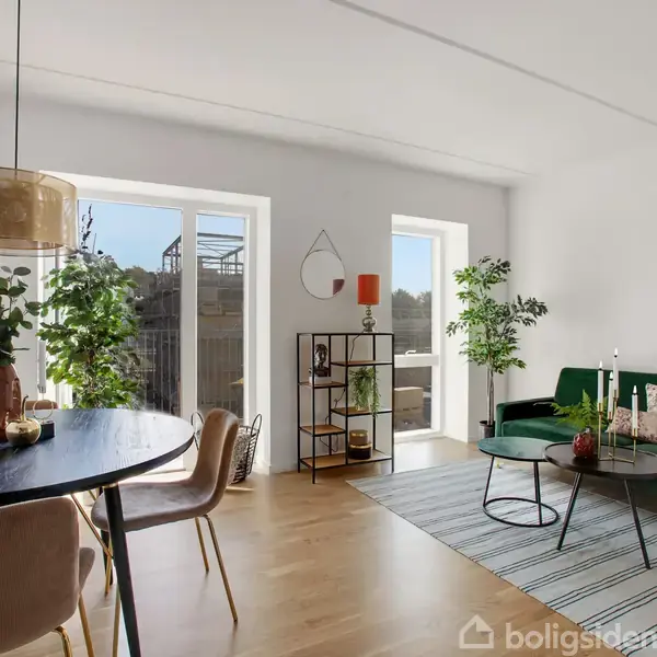 En lys stue med grønt sofabord og sofa med puder. Rundt spisebord til fire foran store vinduer. Planter og få dekorationer skaber en hyggelig atmosfære.