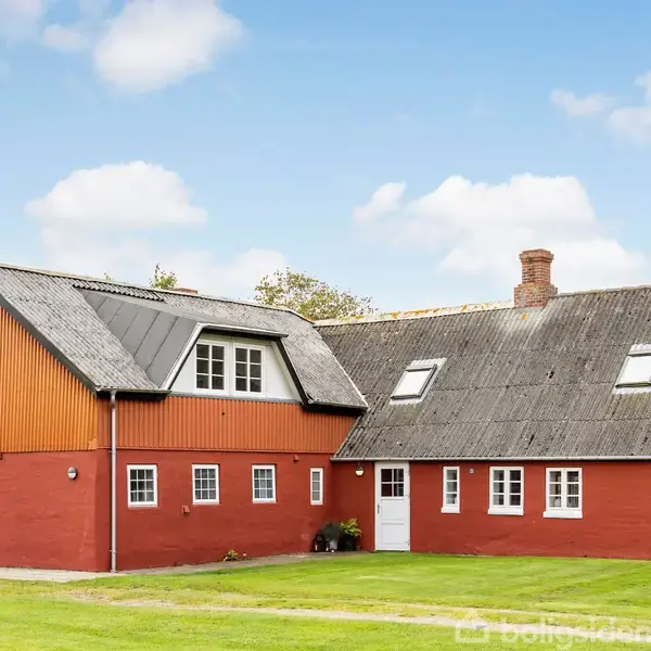 Tofløjet bondegård i rød mursten; ligger stille på en grøn græsplæne med blå himmel og hvide skyer i baggrunden.