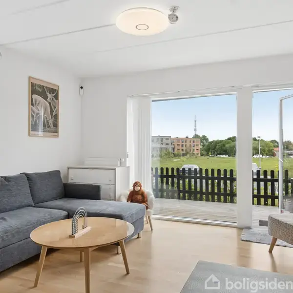 Rækkehus i mursten med sort trægitterhegn foran. Der er en lille have med grønne buske ved indgangen. Bygningens moderne design ses langs en række lignende huse.
