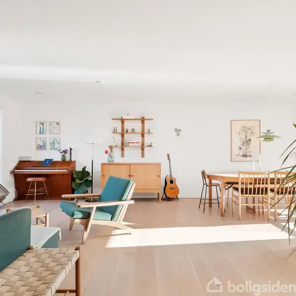Stue med sofa, lænestol og klaver i et lyst og åbent rum. Et spisebord med stole står ved siden af en guitar, omgivet af dekorative hylder og planter.
