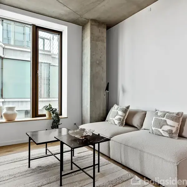 Sofa med lyse puder står foran et stort vindue. Et sofabord i metal og glas er foran sofaen. Potteplanter og pynteting dekorerer vindueskarmen.