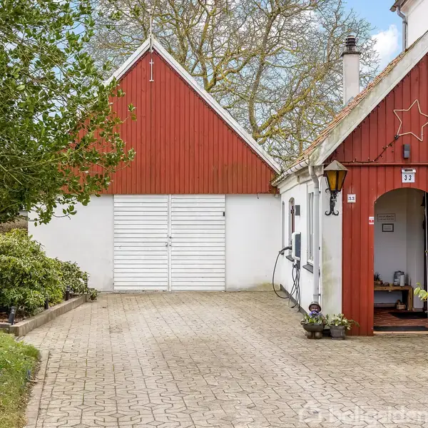 En hvid og rød bygning med en stjerne over indgangsdøren. En stenbelagt indkørsel fører til en garage med hvide porte. Omgivet af træer og buske.
