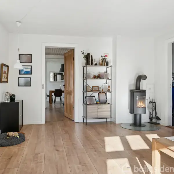 Et rødt murstenshus med mørkt tag står stille i en forstad. Huset har en garage til venstre og en grusbelagt indkørsel. Græsplæne og træer omgiver ejendommen.