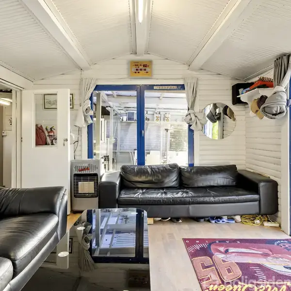 Et rum med to sorte lædersofaer omkring et glasbord. Store vinduer og en åben dør giver udsigt til en terrasse og have. Indretningen er lys med hvide vægge.