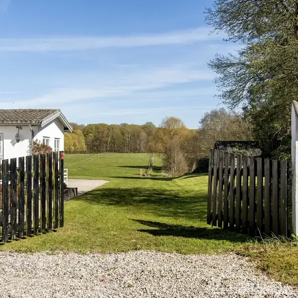 En åben træport fører til en græsmark ved siden af et hvidt hus. Til venstre står skiltet "Enghøj", og til højre ses nummeret "5L".