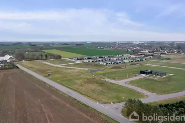 Et stort grønt område med bebyggelse i baggrunden og marker til venstre. Små veje snor sig gennem landskabet. Huse og bygninger kan ses i horisonten.