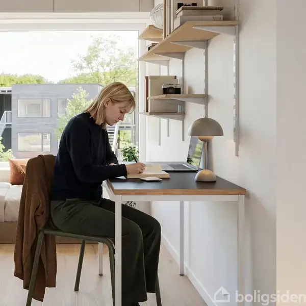 En laptop ligger på en seng ved et stort vindue. Udenfor ses moderne huse og træer i solskin. En plakat med en sol hænger på væggen.
