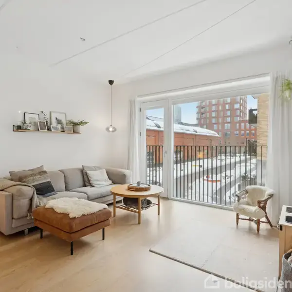 En stue med en grå sofa og brunt bord. Sofaen vender mod store vinduer med udsigt til en sneklædt altan. På væggen hænger et afrikansk-inspireret kunstværk.