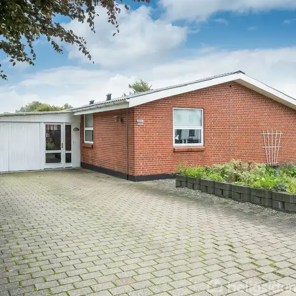 Rødt murstenshus har fladt tag, enkelt vindue og tilstødende carport; flankeret af flisebelagt indkørsel og blomsterbede, beliggende i en boligkvarter. Husnummer "31" vises på skilt.