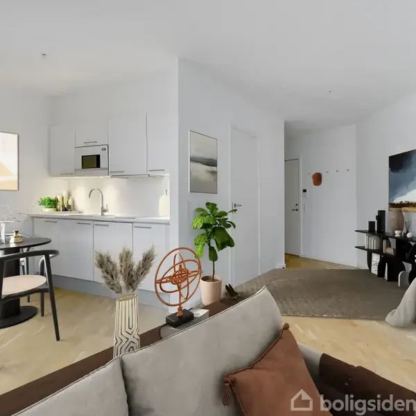 Lejlighedens stue har en sofa og et rundt spisebord. Køkkenet er i hjørnet med hvide skabe. Grønne planter og moderne kunst pryder rummet, der har lyst trægulv.