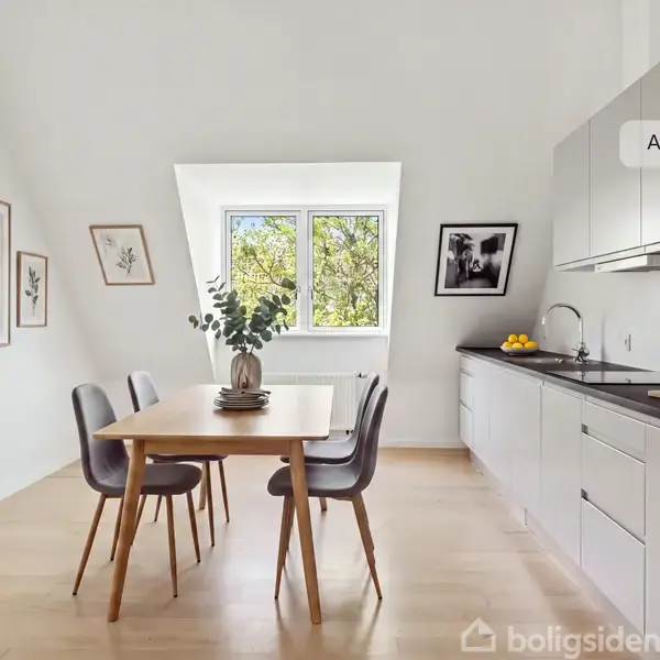 Et lille balkonsæt med to stole og et bord med en vinflaske og glas. Beliggende på en balkon med røde murstensvægge og udsigt over nabotage. Tekst: “AI visualisering”.