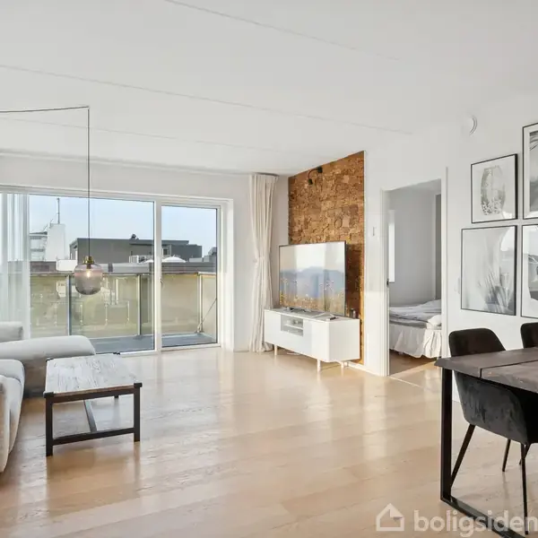 Stue med lys sofa og sofabord til venstre, spisebord til højre. Store glasdøre åbner ud til en altan. Væggene er dekoreret med billeder. Lav tv-reol foran træpanelvæg.