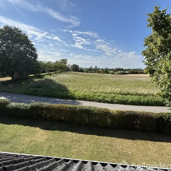 Blå og sorte skabe hænger på en hvid væg i en entre. Trappe fører opad. Dør åbner ud mod en solrig have med græsplæne og buskads.