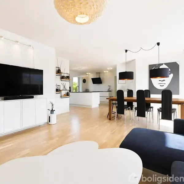 Stue med moderne indretning; fladskærms-TV på væggen, stor spisebord med sorte stole og kunstværk på væggen. Glat trægulv og store vinduer med naturligt lysindfald.