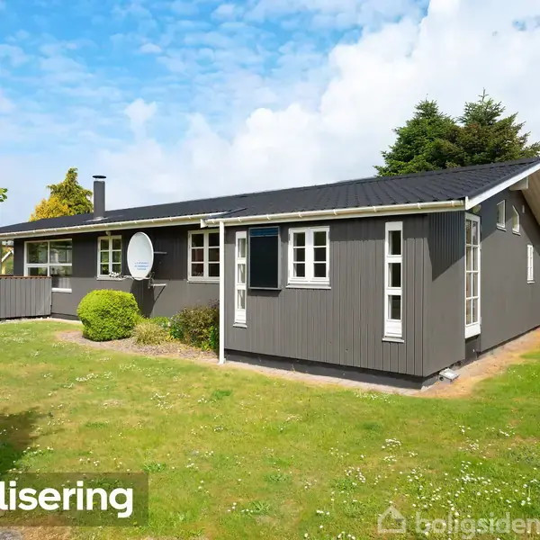 Et gråt træhus med sort tag står på en grøn græsplæne omgivet af buske og træer. Foran huset står teksten "Visualisering".