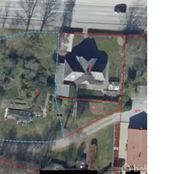 Et satellitbillede viser en ejendom med en villa omgivet af stor have. Røde linjer markerer matrikelgrænserne. En vej ses i nærheden med træer langs kanten.