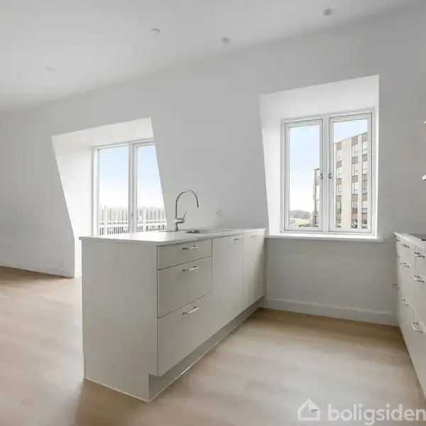 Et lyst køkken med lyse træplanker og hvide skabe med en indbygget ovn. Rummet har store vinduer med udsigt til en bybygning, der giver naturligt lysindfald.