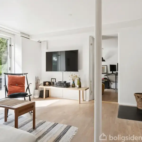Stue med sofa, bord og lænestol ved store glasdøre, der åbner til have. Fladskærms-tv på væggen, moderne brændeovn i hjørnet, kontor i tilstødende rum.