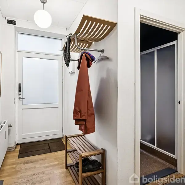 Entreen indeholder en knagerække med en jakke og hylde til hatte. Der er en bænk med sko og en rund loftlampe. Til højre ses en dør til et andet rum.