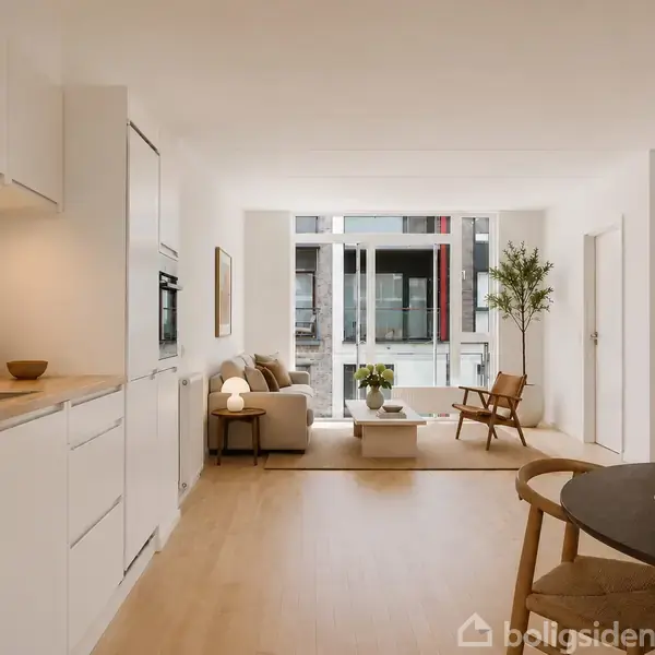 Et moderne køkken-alrum med hvide skabe strækker sig mod en stue med sofa, lænestol og bord. Store vinduer giver udsigt til bygning. Boligsiden vandmærke nederst.