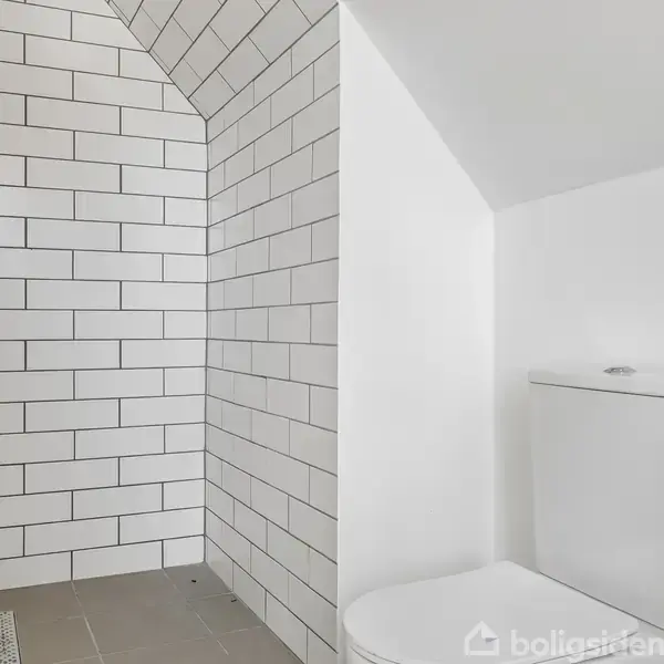 Bruseområde med hvidkalkede mursten på skrånende væg. Ved siden af står et toilet i et rum med hvide vægge.