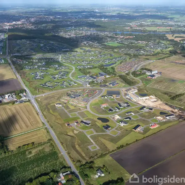 Luftfoto viser nybyggeri med spredte huse og veje i en landlig, landbrugsomgivet landskab. Klare grænser markerer beboelsesområdet mod markerne, der omkranser området.