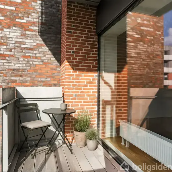 En lille balkon med en stol og et bord står i sollys. Ved siden af er der to planter i potter. Omgivet af murstensbyggeri og en glasvæg.