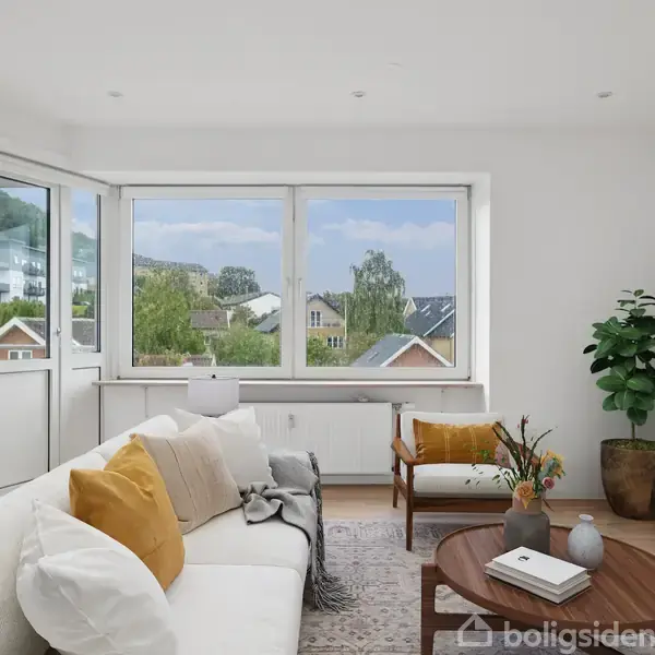 Stue med sofa og puder i aksjon med udsigt til en række huse gennem store vinduer. Der er et træbord med vaser, en stol og en stor grøn plante i potte.