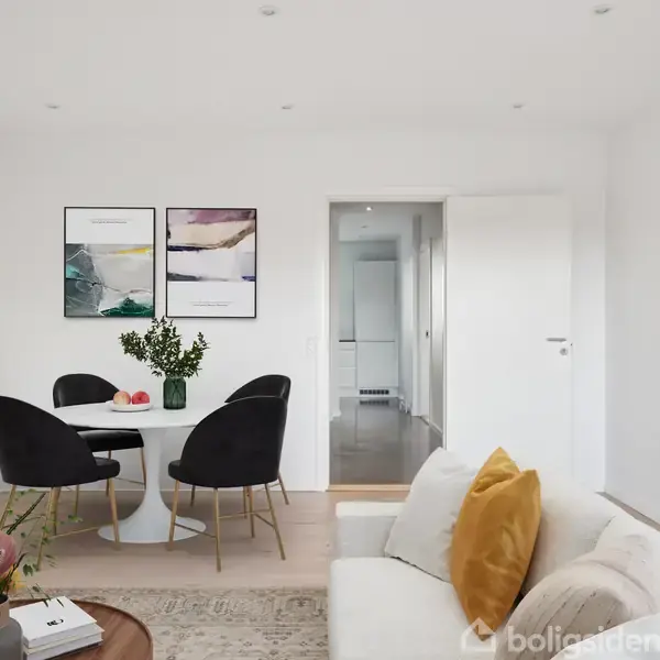 En stue med en hvid sofa med gule puder står overfor et rundt spisebord med sorte stole. Vasen med blomster på bordet tilføjer farve til det minimalistiske rum.