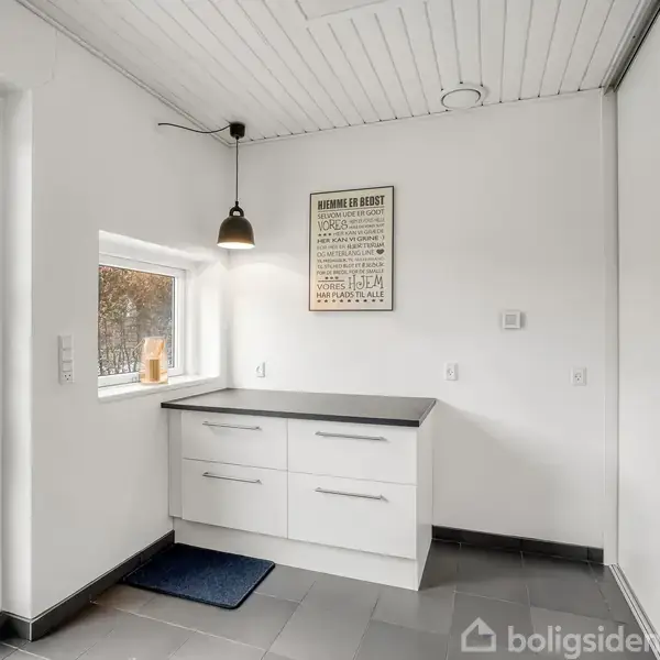 Et hvidt entrérum med moderne skab, hængende lampe og udendørsudsigt gennem glasdør. Plakat på væggen: “Always do your best. Work hard. Never give up. Go big... or go home."