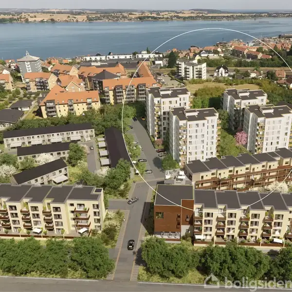 Flere etagebygninger står stille i et boligområde nær en kyst. Bygningerne omgives af grønne områder og naboer med røde tage. Vandet og en by ses i baggrunden.