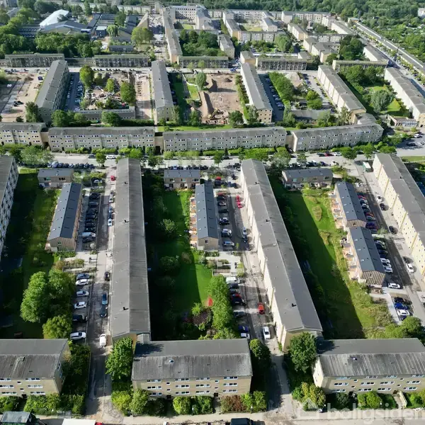 Lejlighedsbygninger i en regelmæssig formation omgivet af træer og grønne arealer. Bygningerne har flade tage og er placeret omkring indre gårde med parkeringspladser og små haver i et byområde.