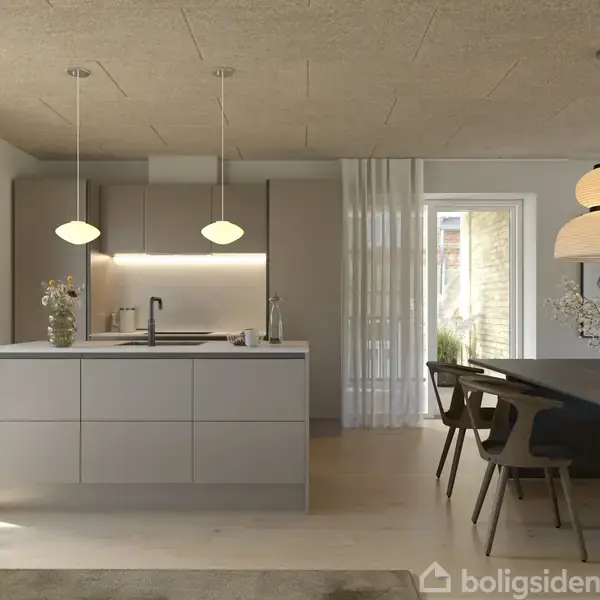Køkken med moderne ø i centrum, hvor to pendellamper hænger over. Til højre står et spisebord med stole. Rummet har høje vinduer og minimalistisk indretning.