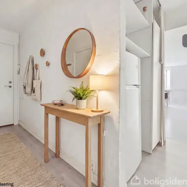 Et lyst entrérum med et lille træbord, dekoreret med en plante, en lampe og et spejl på væggen. Døren til venstre; gang til højre fører til køkken. Tekst: "Visualisering" og "Nybolig AI visualisering".