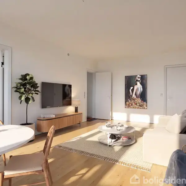 Et lyst stueområde rummer en beige sofa, et rundt sofabord med bøger, et vægmonteret TV, og en plantetop ved siden af. Et kunstværk hænger på væggen.