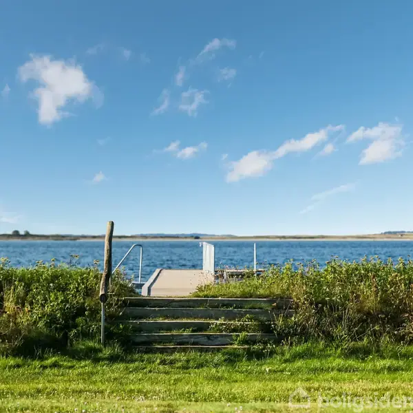 En træbrygge fører til en rolig sø med græs og buske omkring. Himmel med få skyer. Et skilt ved siden af stien viser teksten: "Privat adgang forbudt."