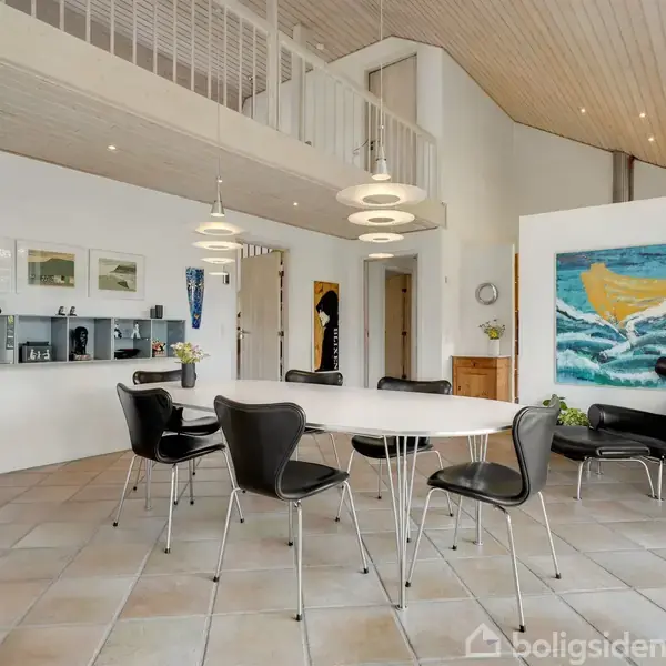 Rundt bord omgivet af sorte stole står på flisegulv i moderne stue. Maleri hænger på væggen ved siden af hylder med pynt. Over bordet hænger moderne lamper.