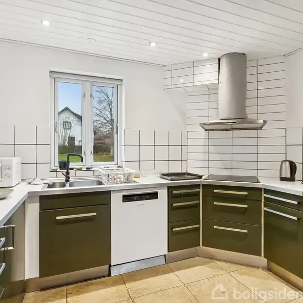 Et moderne køkken har grønne skabe, en indbygget ovn og en mikrobølgeovn. En emhætte hænger over kogepladen. Et vindue i baggrunden giver udsigt til en have.