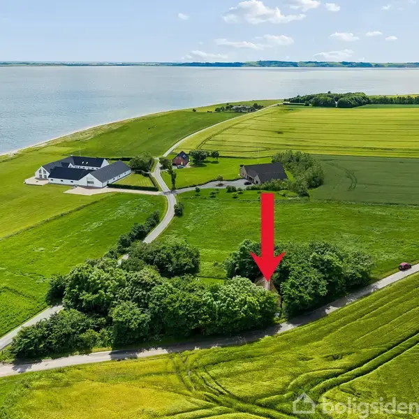 Et rødt huslysspil på åbent grønt landskab nær vandet. Røde pil peger mod træer nær vejen. Omkringliggende marker og bygninger i baggrunden.