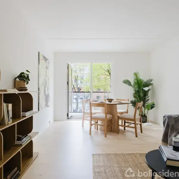 Stue med sofabord og sofa til højre, bøjlereol med bøger og dekorationsspejl til venstre. Rummets baggrund har spisebord med stole ved fransk altan; store vinduer lader lys ind.