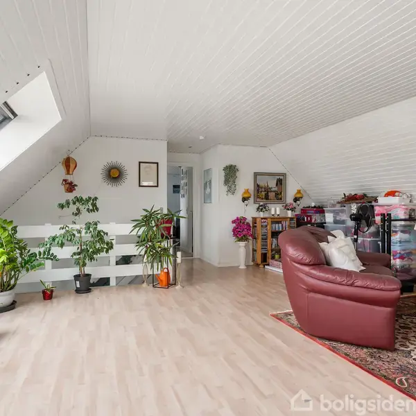 Et lyst loftstueområde indeholder en brun lænestol og planter i potter. Udsmykning med billeder og dekorationer på væggen skaber en hyggelig atmosfære.
