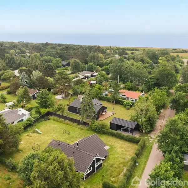 En række enfamiliehuse ligger spredt i en skovklædt, kystnær landsby. Det rolige miljø er præget af grønne områder og en beliggenhed tæt på havet i horisonten.