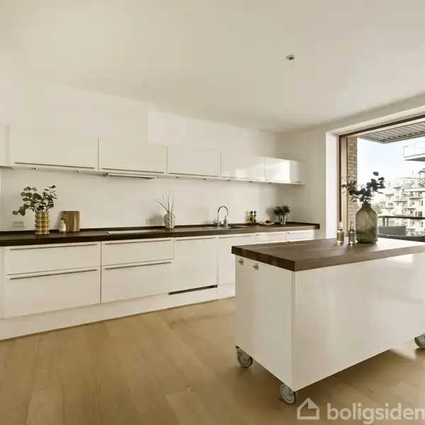 Et moderne køkken med hvide skabe og skuffer. En mobil køkkenø står midt på det lyse trægulv. Udsigt til en balkon og moderne bygninger udenfor store vinduer.