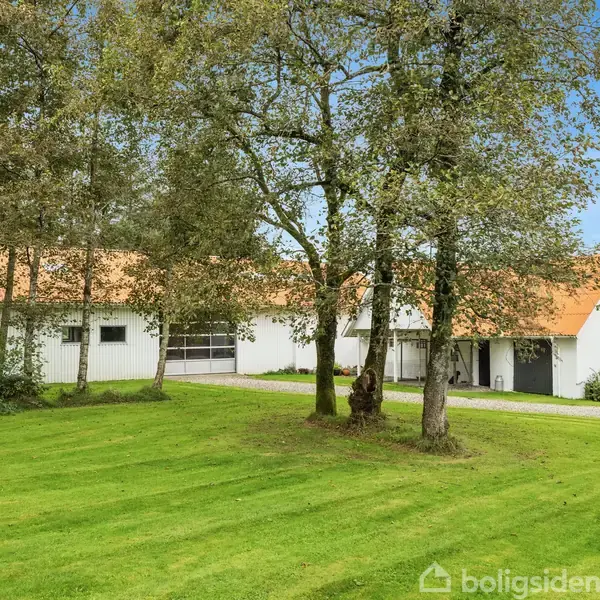 En hvid bygning med rødt tag står fredfyldt bag nogle træer. Foran bygningen er en veltrimmet græsplæne i et grønt, landligt område.