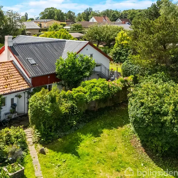 Et hus omgivet af en frodig have. Taget er delvist dækket af solpaneler. Huset ligger i et villakvarter med grønne træer og buske omkring.