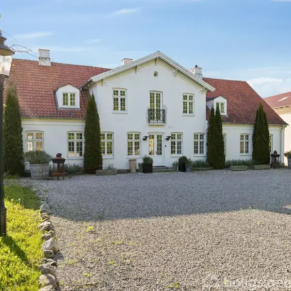 En mørkebrun træbord står i et lyst køkken med hvidt interiør. Tre hvide lamper hænger over bordet, og et parketgulv strækker sig i rummet.