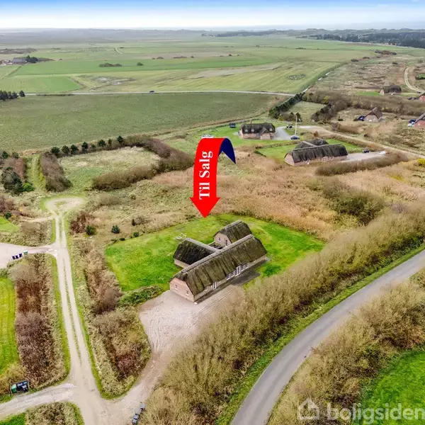 Hus med stråtag markeret af en rød pil med teksten "Til salg". Det ligger i et landligt område med marker, veje og få andre huse omkring.