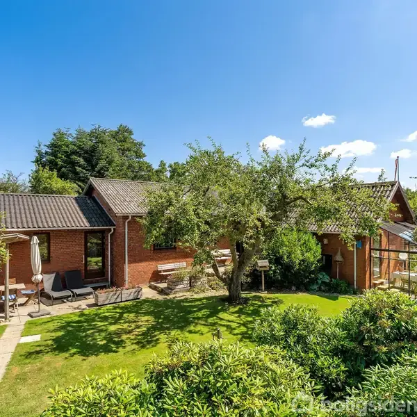 Et rummeligt bibliotek viser en reol fyldt med bøger. Et bord med to stole står i midten, under en loftslampe. Vinduet lader naturligt lys ind i rummet.