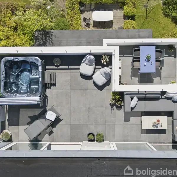 Altan med jacuzzi fyldt med vand, omgivet af stole og borde på en flisebelagt terrasse. Området er omkranset af hække og grønne planter.