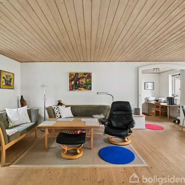 Køkken med hvid flisegulv og træloft, indeholdende hvidevarer som køleskab og emhætte. Køkkenbord med redskaber og en dør åbner ud til en terrasse med træoverdækning.